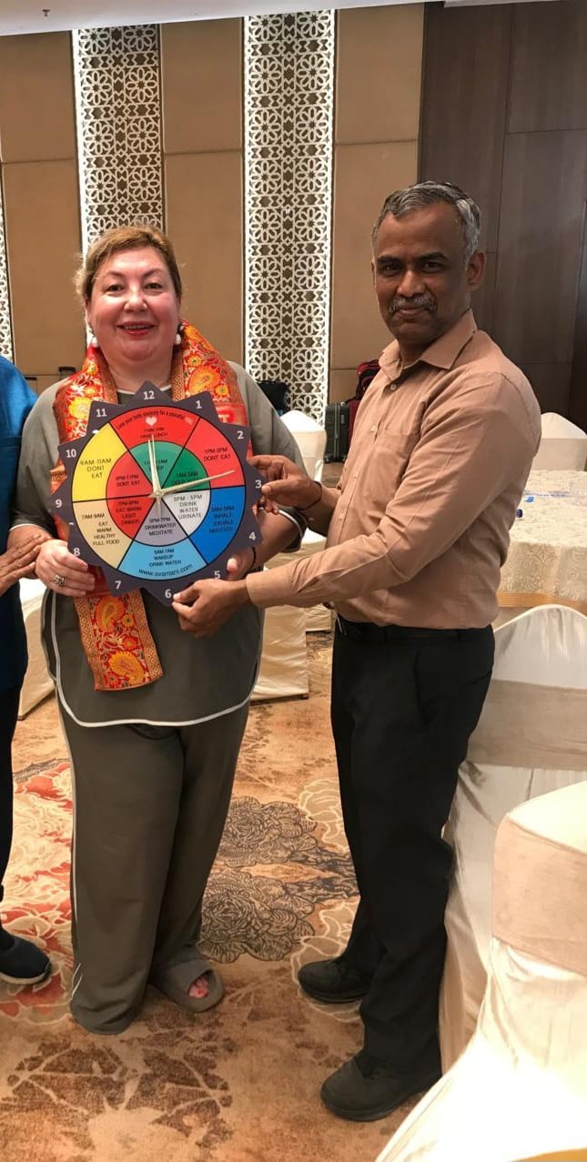 SVS Mani handing his physical colour-coded Organ Clock to a Russian acupuncturist at NSAAI 2025 as a symbol of India-Russia acupuncture friendship